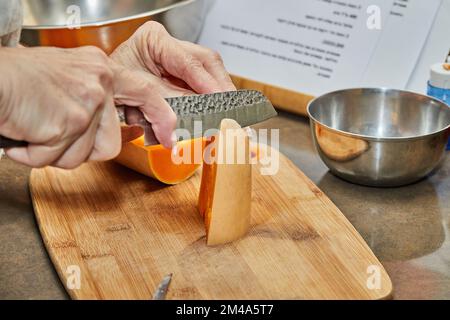 Der Koch schneidet Kürbis in Birnenform auf Holzbrett in der Küche Stockfoto