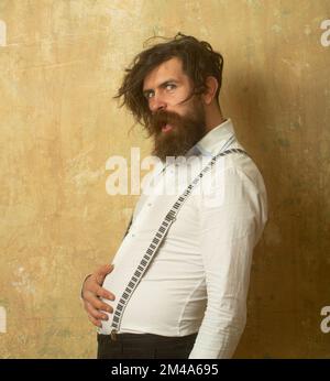 Komischer bärtiger Mann mit ungekämmtem, geschwungenem Haar, der ihren Bauch hält. Stockfoto