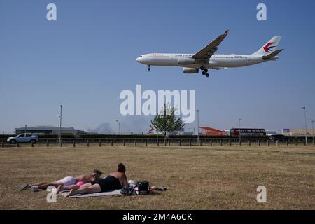 PA REVIEW OF THE YEAR 2022 File Photo dated 19/07/22 - Ein Paar Sonnenbaden, während ein China Eastern Flug auf dem Heathrow Airport, London, landet, wo der heißeste Tag in Großbritannien aufgezeichnet wurde, mit einer Temperatur von 40,2C °C nach vorläufigen Zahlen des MET Office. Ausgabedatum: Dienstag, 20. Dezember 2022. Stockfoto