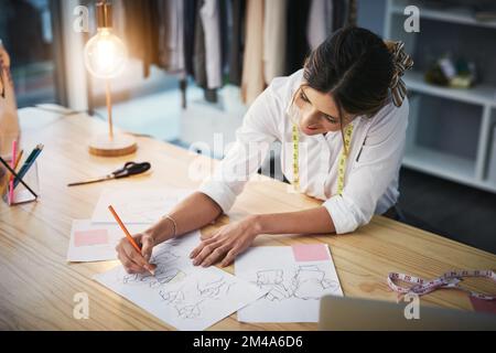 Seine Kreativität in Aktion. Ein Foto aus dem Blickwinkel einer attraktiven jungen Modedesignerin, die in ihrer Werkstatt an ihren Entwürfen arbeitet. Stockfoto