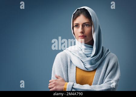 Sie hat viel um die Ohren. Eine attraktive junge Frau, die aufmerksam aussieht, während sie vor grauem Hintergrund posiert. Stockfoto