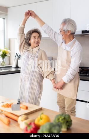 Fröhliches chinesisches Seniorenpaar, das in der Küche tanzt Stockfoto