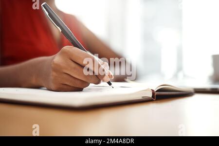 Dinge zu Hause erledigen. Eine unbekannte Geschäftsfrau, die sich Notizen in ihr Notizbuch in ihrem Heimbüro schreibt. Stockfoto