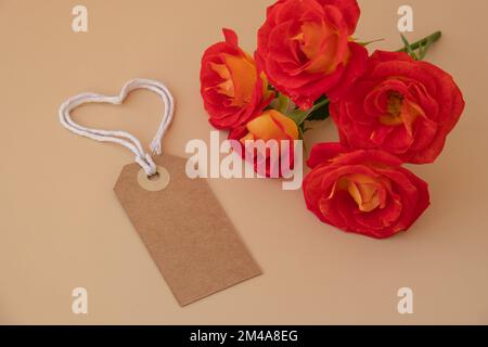 Einfarbige beige Papiernote und Seil in Herzform auf neutralem beigen Hintergrund. Zarte rote Rosen Grußkarte Feiertagsidee. Erstellen Sie einen Kopierplatz für Text. Geschenk Stockfoto