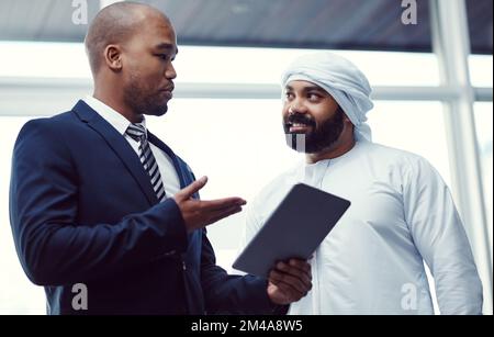 Um Ergebnisse zu erzielen. Zwei Geschäftsleute, die ein digitales Tablet verwenden, während sie ein Gespräch in einem modernen Büro führen. Stockfoto