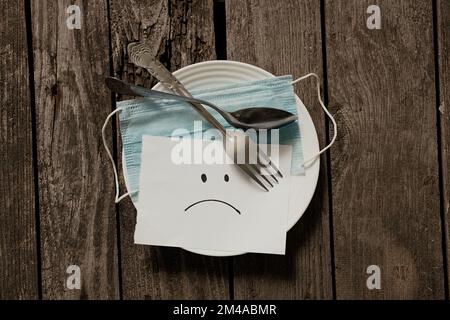 Medizinische Maske trauriges Emoticon auf weißem Papier auf einem Tisch gemalt Stockfoto
