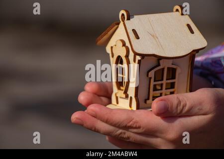 Die Kinderhand hält ein kleines Holzhaus auf einem verschwommenen Hintergrund Stockfoto