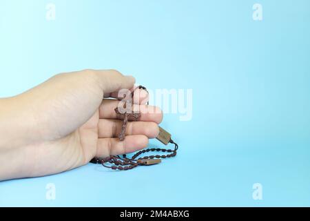 Menschliche Hand betet und hält einen skapularen Rosenkranz auf blauem Hintergrund. Christentum und Katholizismus. Stockfoto