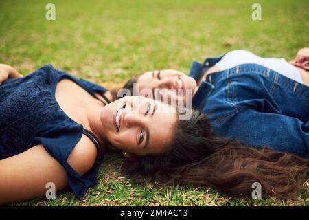 Unsere Freundschaft ist für immer. Zwei weibliche beste Freunde, die auf dem Rasen in einem öffentlichen Park liegen. Stockfoto