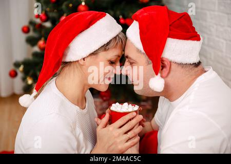 Süßes junges Paar, das heisse Schokolade am Heiligabend zu Hause trinkt. Stockfoto