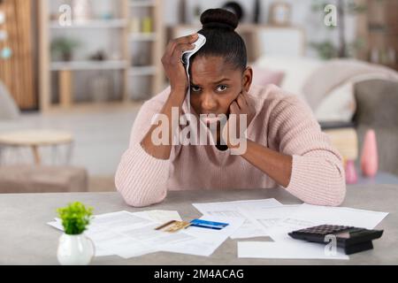 Deprimierte Frau, die Rechnungen ansieht und ihren Kopf hält Stockfoto