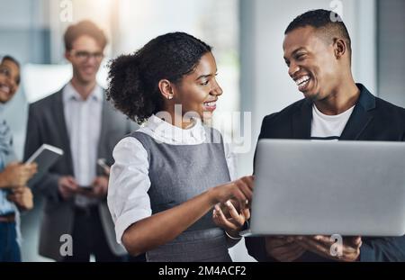 Ich bin froh, dass wir uns da einig sind. Eine Gruppe junger, fröhlicher Geschäftsleute, die auf digitalen Geräten surfen, während sie im Büro zusammenarbeiten. Stockfoto