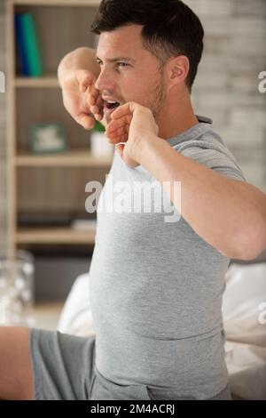 Ein Mann wacht im Bett auf und streckt sich Stockfoto