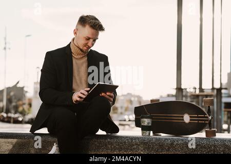 Eleganter Skater mit einem Tablet, das in einem Quadrat sitzt Stockfoto