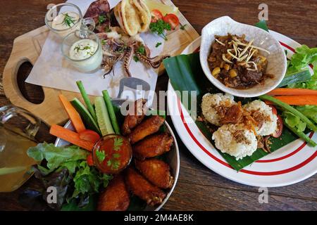 Gebratener klebriger Reis serviert mit northailändischem Curry, Hähnchenflügeln und gebratenem, frittierten Calamari-Tintenfisch Stockfoto