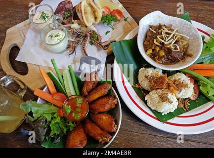 Gebratener klebriger Reis serviert mit northailändischem Curry, Hähnchenflügeln und gebratenem, frittierten Calamari-Tintenfisch Stockfoto