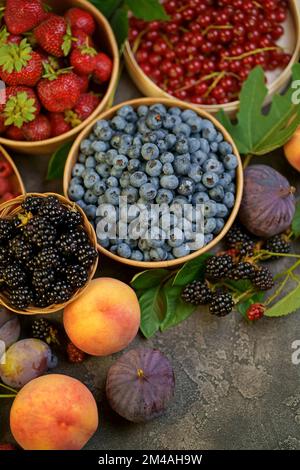 Mix aus frischen Beeren mit Blättern in Vintage-Holzkiste auf rustikalem Holzhintergrund. Draufsicht. Rohe, gesunde Lebensmittel. Verschiedene Beeren. Stockfoto