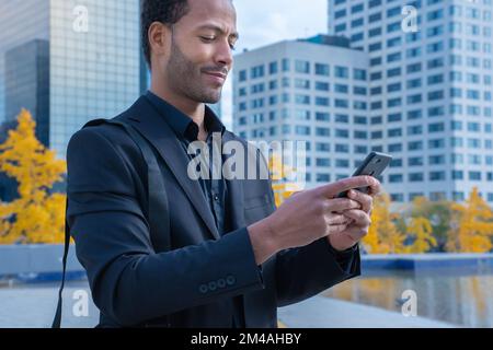 Schwarzer Geschäftsmann, der außerhalb des Büros in der Stadt SMS mit einer Mobiltelefon-App schickt. Stockfoto