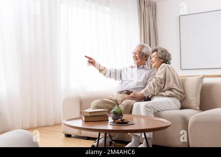 Fröhliches chinesisches Seniorenpaar, das auf dem Sofa sitzt Stockfoto