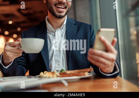 Ein lächelnder indischer Geschäftsmann im Anzug telefoniert während der Mittagspause im Café. Unscharfer Hintergrund Stockfoto