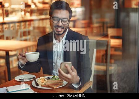 Ein lächelnder indischer Geschäftsmann im Anzug telefoniert während der Mittagspause im Café. Unscharfer Hintergrund Stockfoto