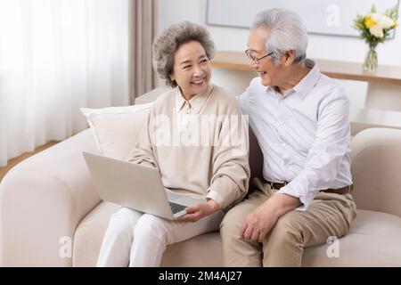 Fröhliches chinesisches Seniorenpaar, das zu Hause ein Laptop benutzt Stockfoto