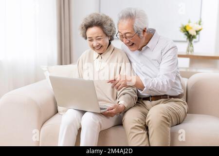 Fröhliches chinesisches Seniorenpaar, das zu Hause ein Laptop benutzt Stockfoto