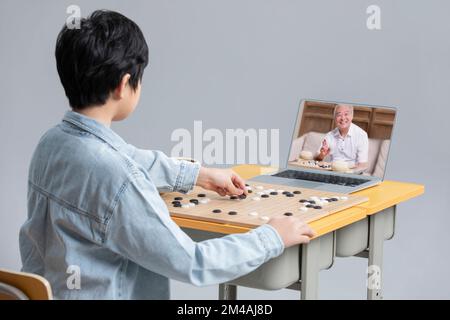 Süßer chinesischer Junge, der das Go-Spiel mit einem Laptop lernt Stockfoto