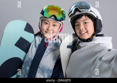 Fröhliches chinesisches Mädchen und Junge mit Snowboards Stockfoto