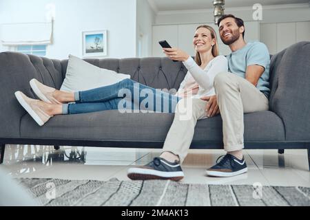Paare, Sofa und entspannen Sie sich mit tv-Fernbedienung, Lächeln und Glück im Wohnzimmer, um sich mit Liebe zu verbinden. Glückliches Paar, Couch und Comedy im Fernsehen Stockfoto