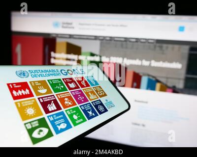 Smartphone mit Logo der UN Sustainable Development Goals (SDG) auf dem Bildschirm vor der Website. Fokus auf die Mitte rechts des Telefondisplays. Stockfoto