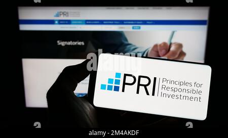Person, die ein Mobiltelefon mit dem Logo der UN Principles for Responsible Investment (PRI) auf dem Bildschirm vor der Webseite hält. Konzentrieren Sie sich auf das Display des Telefons. Stockfoto