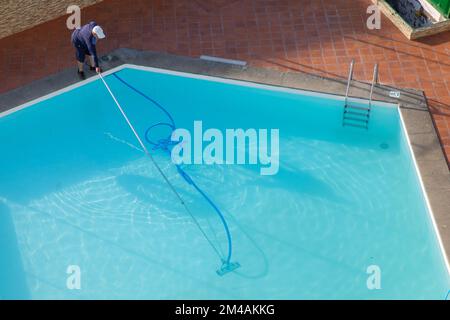 Mann, der den Swimmingpool mit Staubsaugergeräten reinigt. Poolreinigung. Ein Mann putzt den Pool. Service-Pflege. Stockfoto