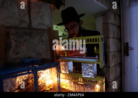 Jerusalem. 19.. Dezember 2022. Ein Mann zündet am 19. Dezember 2022 in Jerusalem in der ultra-orthodoxen jüdischen Gemeinde Mea Shearim Kerzen für das Festival von Hanukka an. Kredit: Gil Cohen Magen/Xinhua/Alamy Live News Stockfoto