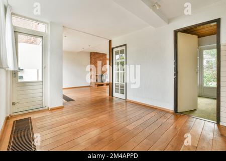 Leeres modernes Zimmer neben hellen Fenstern und Parkettboden mit einem Kamin im Hintergrund Stockfoto