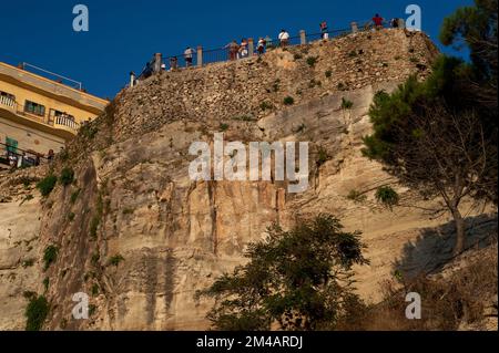 In der goldenen Abendsonne ruhen sich Urlauber an den Geländern eines belvedere über erodierten Sandsteinklippen aus, die die Altstadt von Tropea an der Westküste Kalabriens, Süditalien, stützen. Der Aussichtspunkt bietet einen spektakulären Blick auf das türkisfarbene Tyrrhenische Meer. Stockfoto