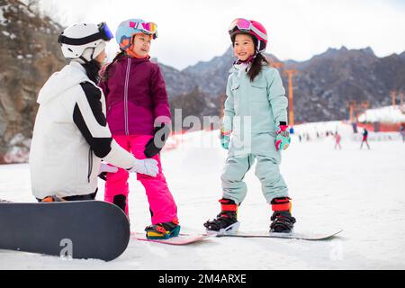 Chinesische Kinder lernen mit ihrem Trainer Snowboarden Stockfoto