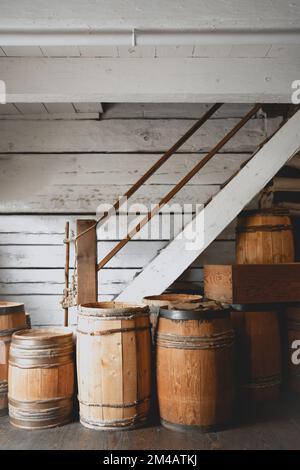 Eine vertikale Aufnahme alter rustikaler Weinfässer unter der weißen Holztreppe im Keller Stockfoto