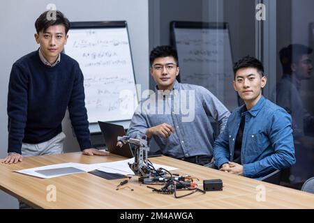 Selbstbewusste chinesische Konstrukteure überprüfen einen Roboterarm Stockfoto