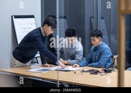 Selbstbewusste chinesische Konstrukteure überprüfen einen Roboterarm Stockfoto