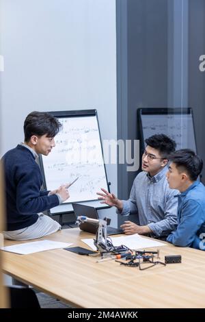 Selbstbewusste chinesische Konstrukteure überprüfen einen Roboterarm Stockfoto