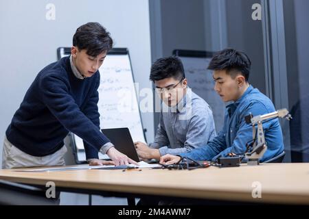 Selbstbewusste chinesische Konstrukteure überprüfen einen Roboterarm Stockfoto