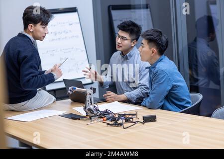 Selbstbewusste chinesische Konstrukteure überprüfen einen Roboterarm Stockfoto