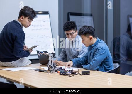 Selbstbewusste chinesische Konstrukteure überprüfen einen Roboterarm Stockfoto