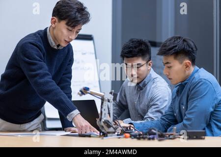 Selbstbewusste chinesische Konstrukteure überprüfen einen Roboterarm Stockfoto