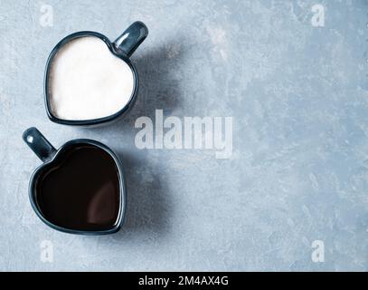 Zwei Tassen in Herzform mit frisch gebrühtem aromatischem Kaffee mit Milch und Espresso auf blauem Hintergrund. Das Konzept der gegensätzlichen Getränke. Draufsicht Stockfoto