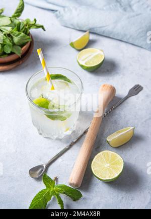 Ein Glas Limettenmojito auf dem Tisch mit Limettenscheiben, Entsafter, Löffel und Minze. Bild in der Draufsicht Stockfoto
