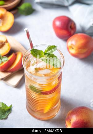 Kalter Pfirsichtee mit Minze und Eis in einem Glas auf blauem Hintergrund. Draufsicht und Nahaufnahme Stockfoto