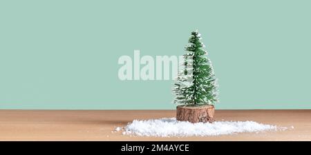 Kleiner dekorativer, verschneiter Weihnachtsbaum vor grünem Hintergrund. Stockfoto
