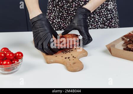 Ein Typ packt getrocknetes Fleisch in Papierkartons mit schwarzen Handschuhen. Hochwertiges Foto Stockfoto